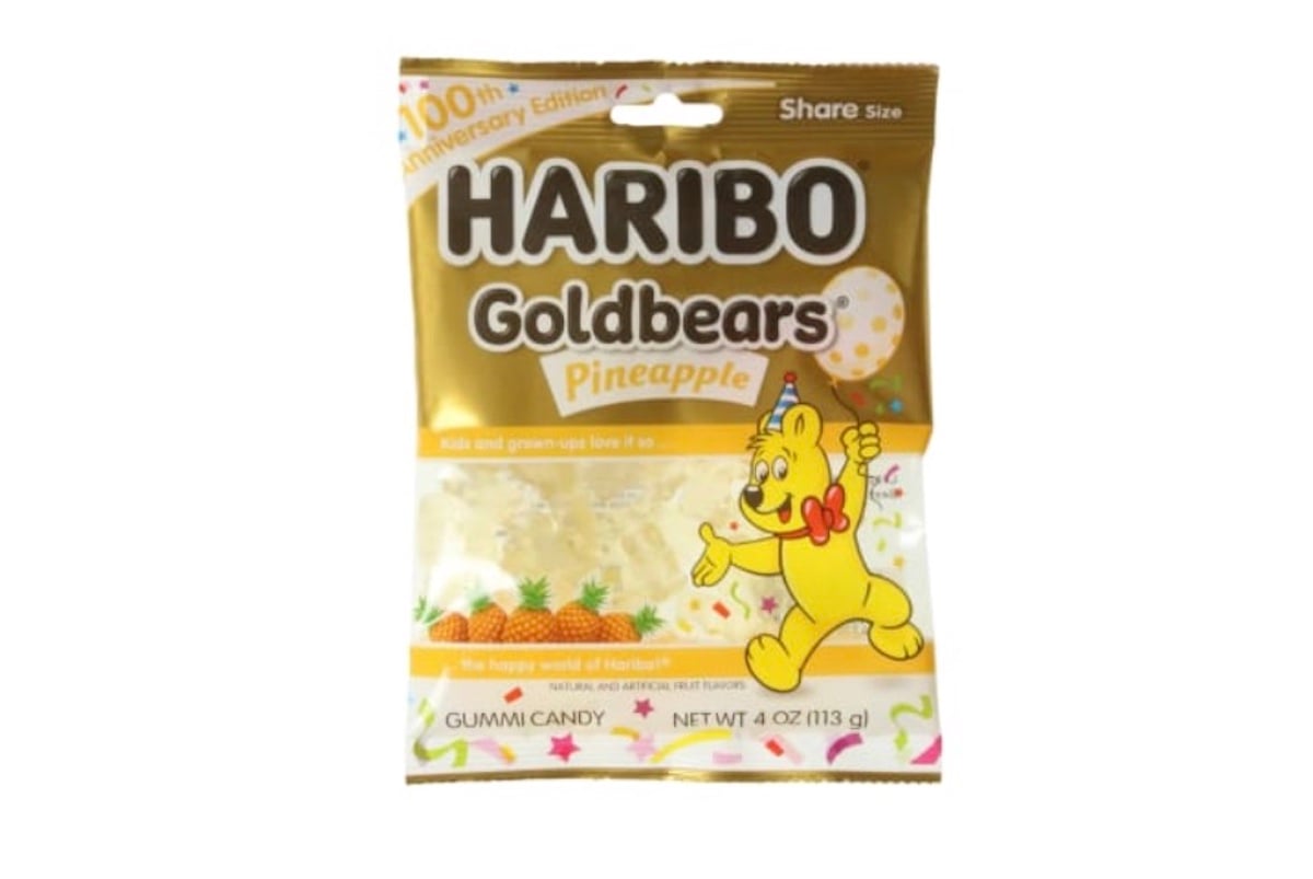 A gold and white bag of HARIBO Goldbears Pineapple gummy candy featuring a cartoon bear holding a pineapple. The bag is labeled "100th Anniversary Edition" and contains 4 oz (113g).