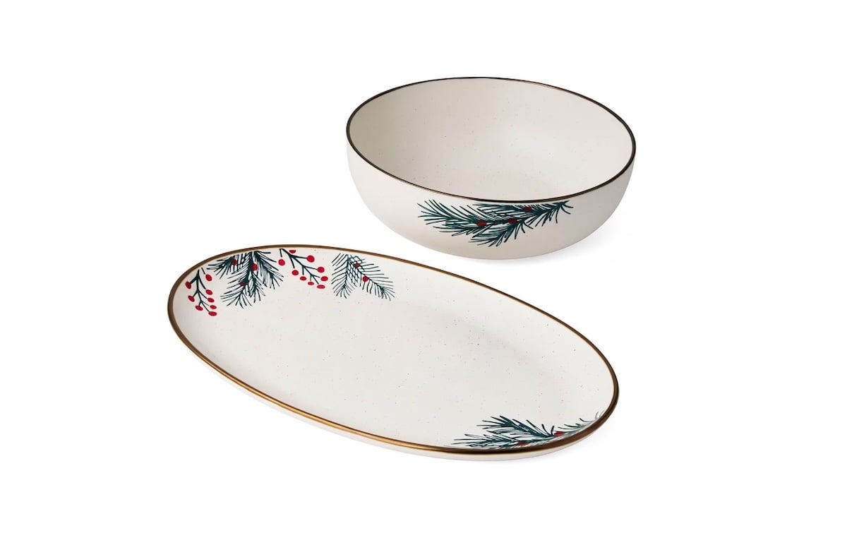 A white ceramic bowl and oval plate with gold rims, each decorated with painted green pine needles and red berries.