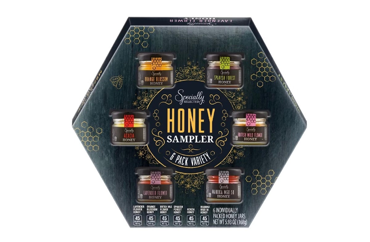 Hexagonal box with six jars of honey sampler by Specialty, each labeled with a different flavor: Pure Honey, Lemon Honey, Orange Blossom Honey, Clover Honey, Wildflower Honey, and Acacia Honey.