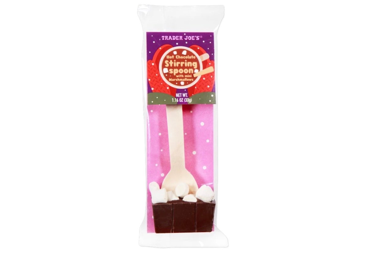 A Trader Joe’s Hot Chocolate Stiring Spoon with mini marshmallows, packaged in a clear wrapper. The chocolate block holds a wooden spoon, and the label is purple and red with white and yellow text.