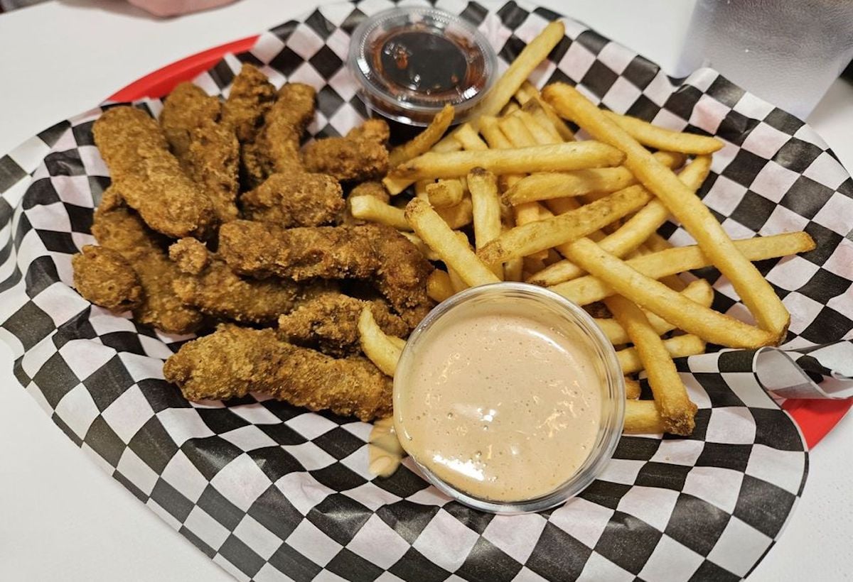 A red tray with black-and-white checkered paper holds crispy chicken tenders, French fries, and two dipping sauces in clear plastic cups—a classic find at many under-the-radar restaurants.