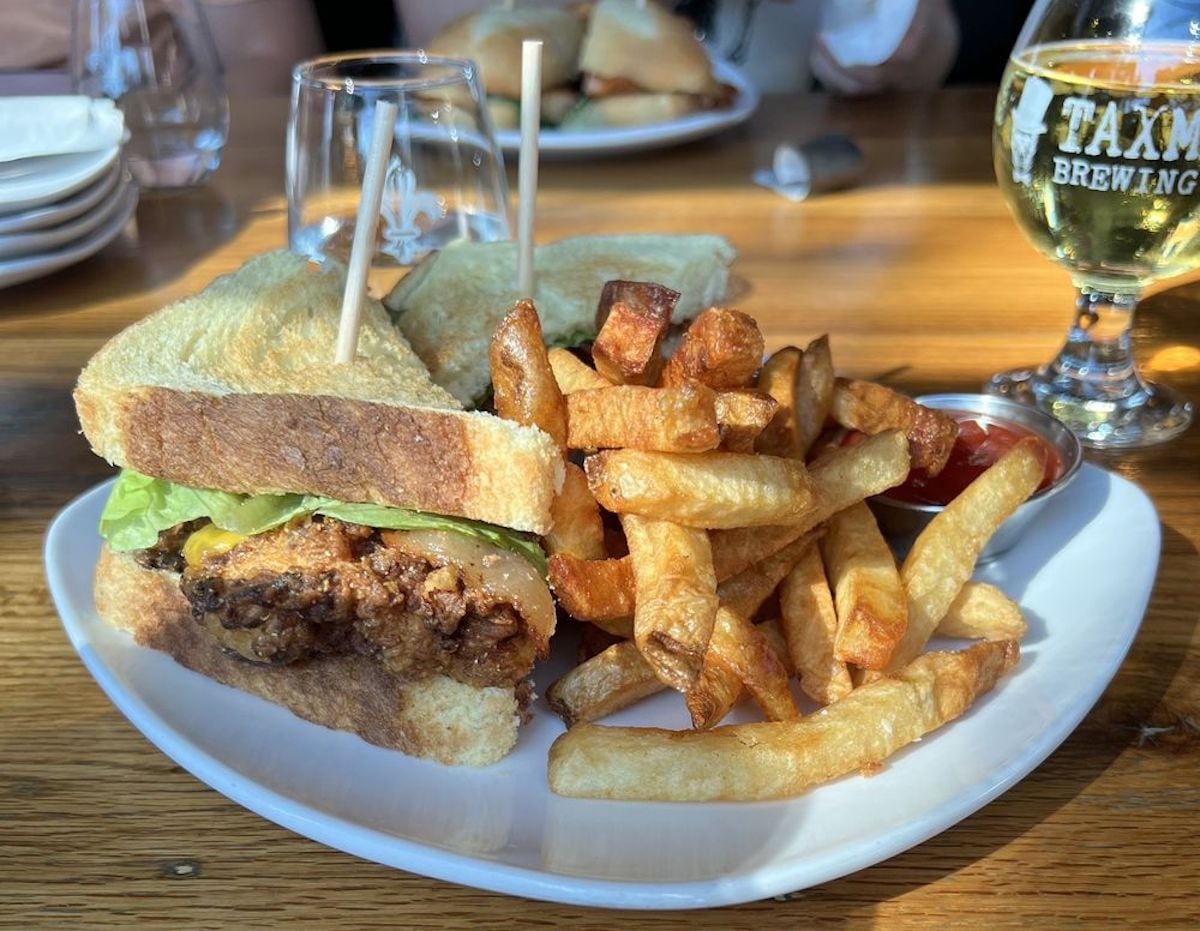 A plate with a fried chicken sandwich on toasted bread, topped with lettuce, sits beside thick-cut fries and ketchup—an inviting meal often found at under-the-radar restaurants—on a wooden table with drinks in the background.