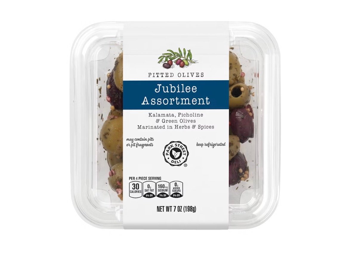 Clear plastic container labeled “Jubilee Assortment” with pitted Kalamata, Picholine, and green olives marinated in herbs and spices. Nutrition info, olives illustration, and “keep refrigerated” message are visible on the label.
