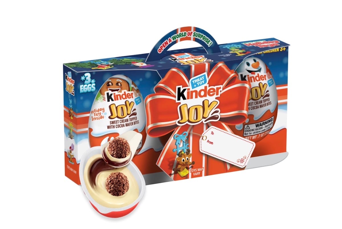 A Kinder Joy gift pack with a festive design, featuring three eggs, a large red bow, and images of the chocolate treat and toy surprises inside. The package includes an open egg showing creamy layers and chocolate balls.