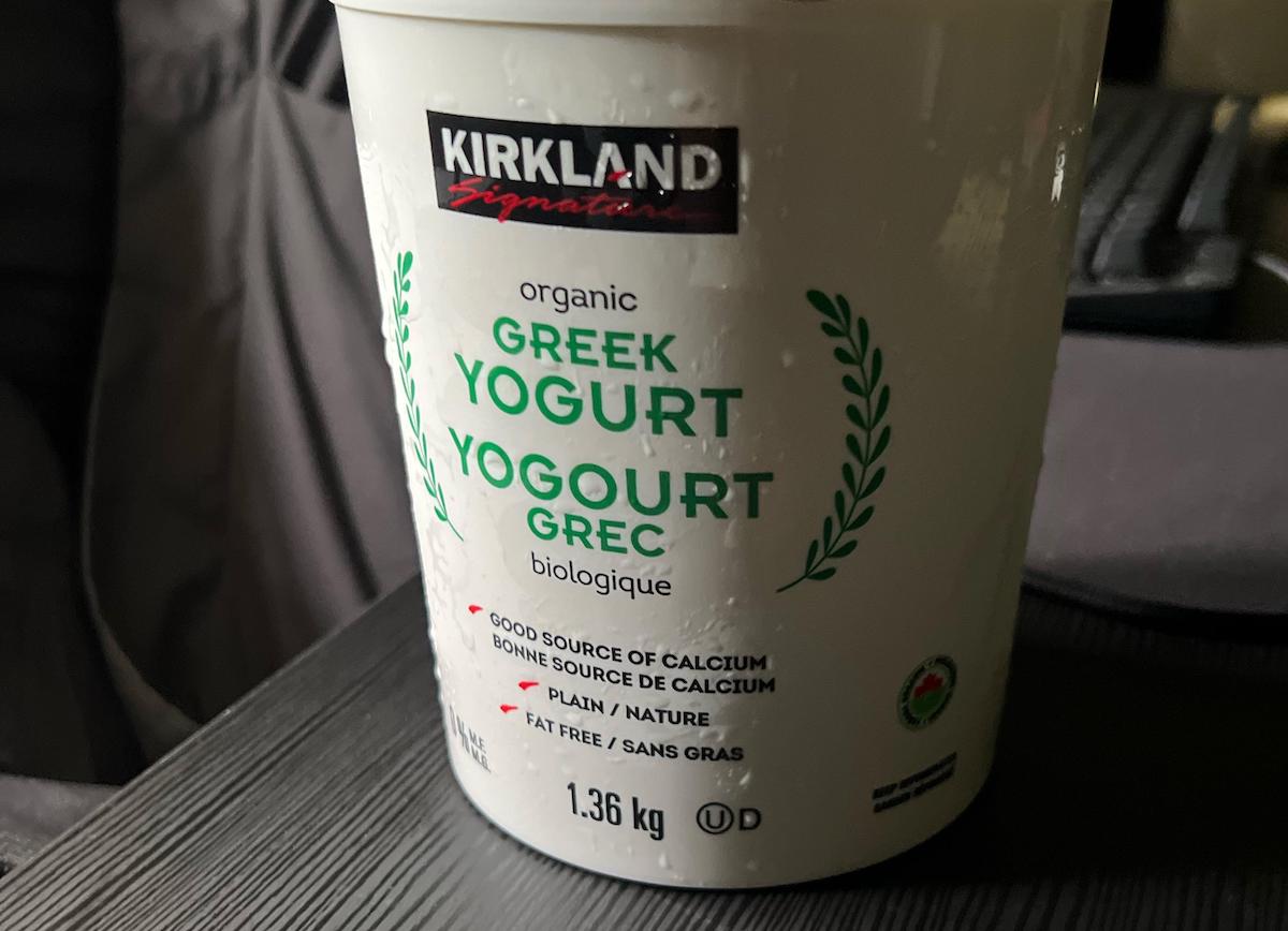 A container of Kirkland Signature organic Greek yogurt, plain and fat-free, weighing 1.36 kg. The label highlights it as a good source of calcium and features bilingual English and French text.