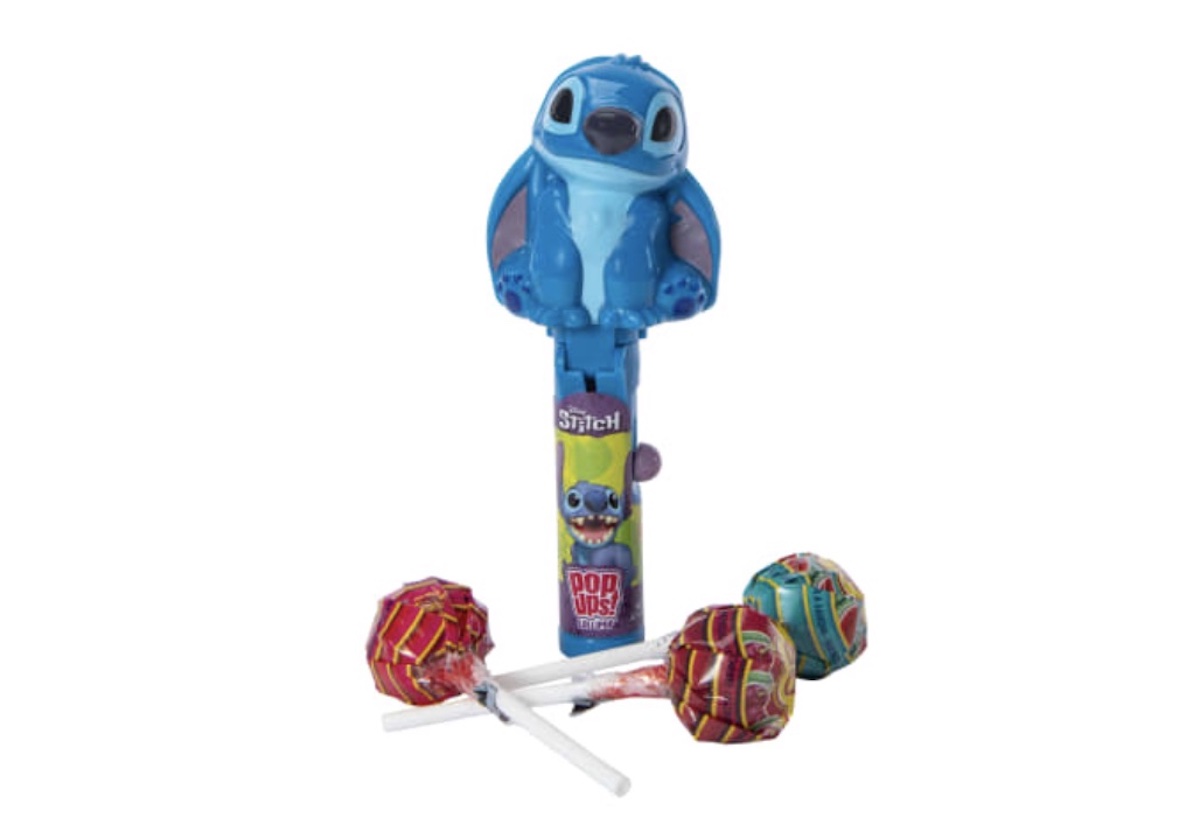 A blue Stitch-themed PEZ dispenser stands upright with four colorful lollipops lying in front of it on a white background.