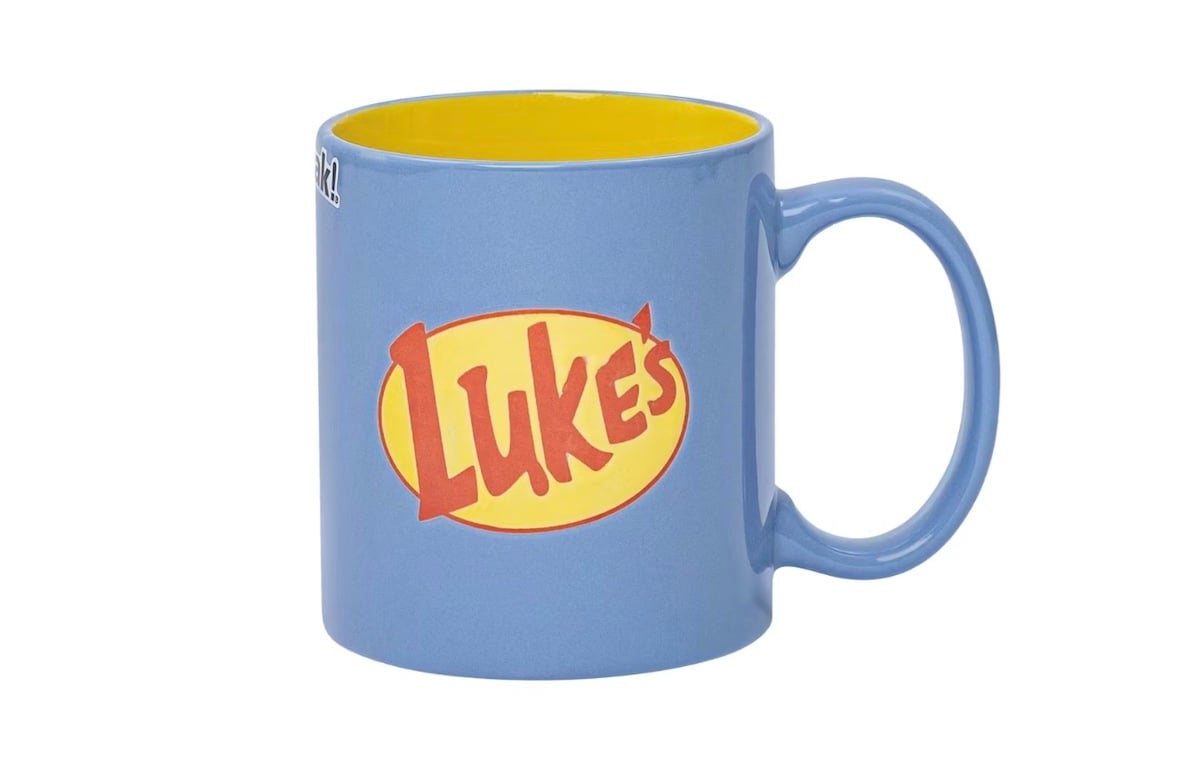 A blue coffee mug with a yellow interior and the word "Luke's" in red, stylized text on a yellow oval background, referencing the café from the TV show "Gilmore Girls.