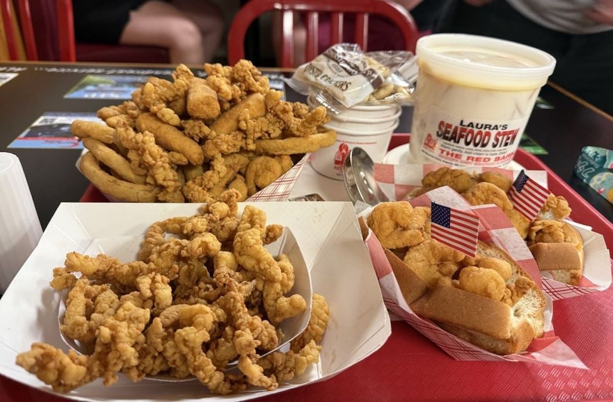 A tray of fried seafood, clam strips, two mini sandwiches with American flags, oyster crackers, a tub of seafood stew, and dipping sauces—classic fare at one of the city’s best under-the-radar restaurants—with red chairs in the background.