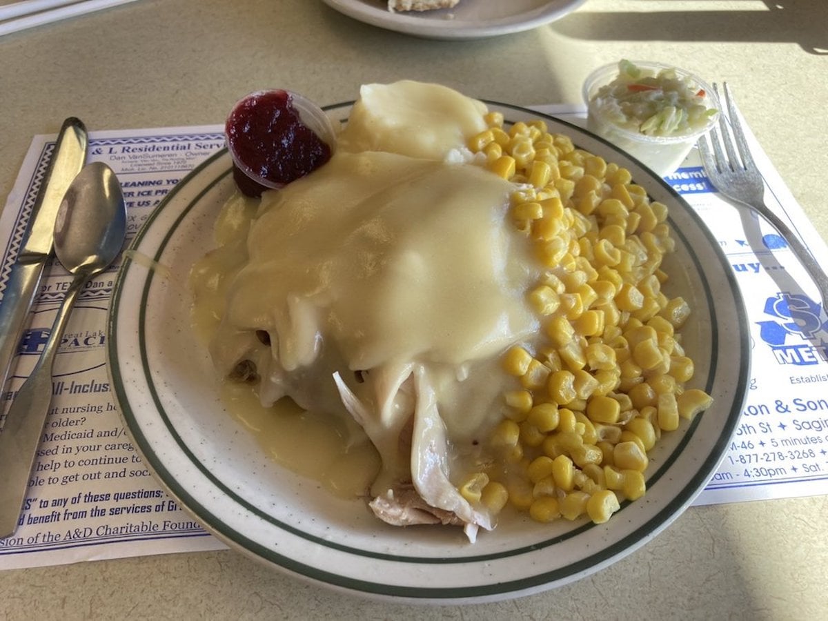 A plate with sliced turkey covered in gravy, yellow corn, cranberry sauce, and coleslaw sits on a cream and green rimmed plate—just the kind of hearty meal you'd find at under-the-radar restaurants.