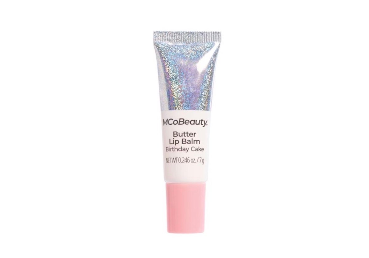 A tube of MCoBeauty Butter Lip Balm in the "Birthday Cake" flavor, featuring a shiny holographic cap and a light pink base, standing upright against a white background.