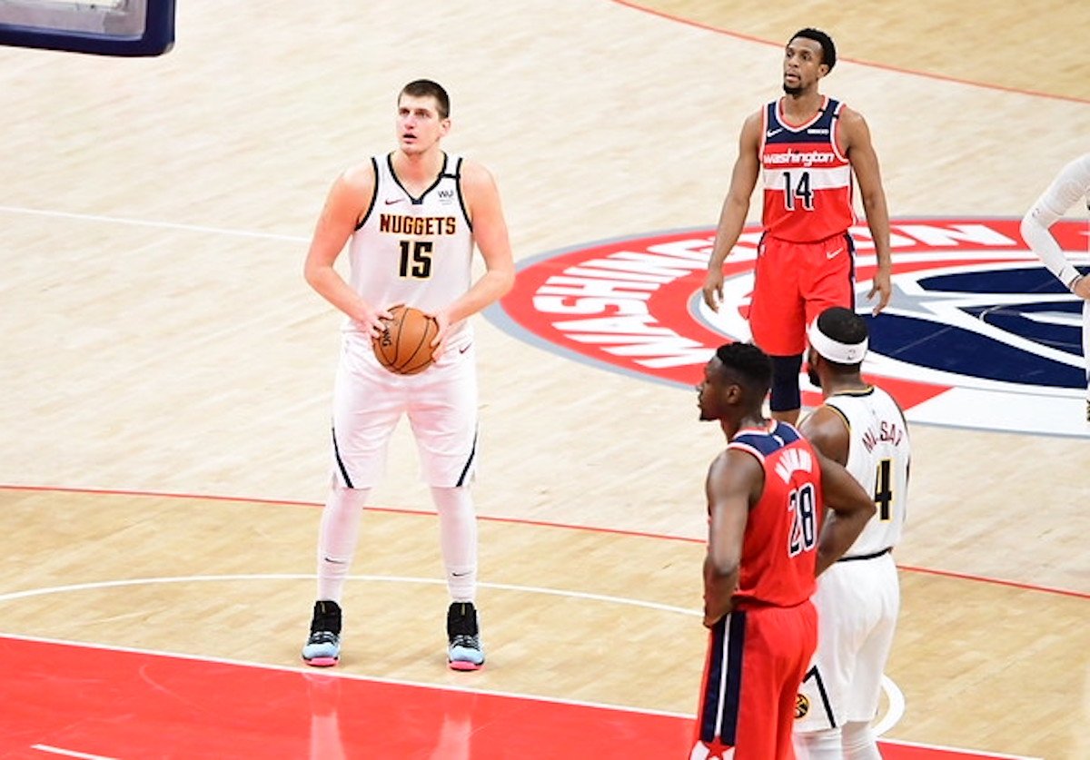 A Denver Nuggets player prepares to shoot a free throw during a basketball game, while Washington Wizards players and another Nuggets teammate stand around the key.