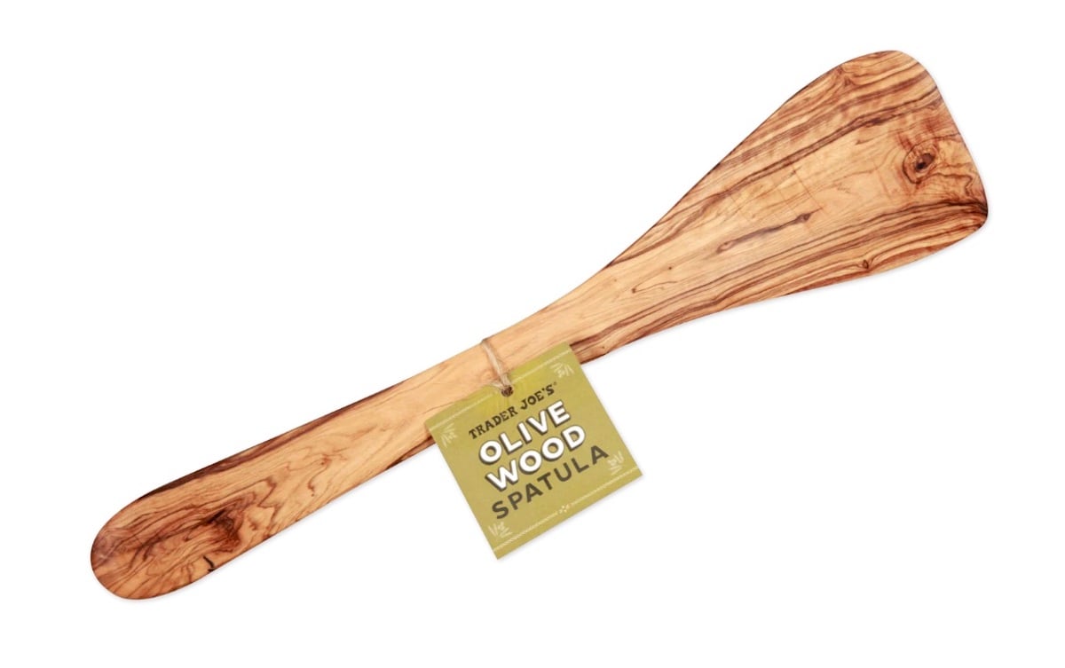 A smooth olive wood spatula with a wide, flat end and a narrow handle, featuring a green label reading "Trader Joe's Olive Wood Spatula" attached to the handle.
