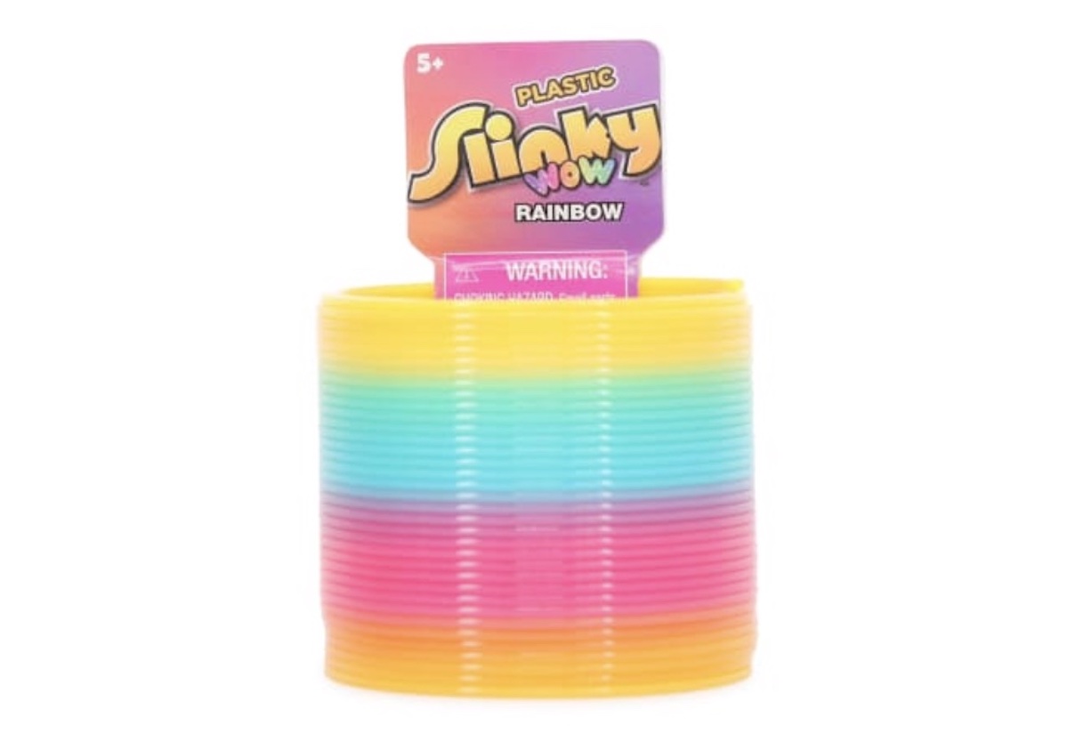 A colorful plastic rainbow Slinky toy in packaging labeled "Slinky Wow" with stripes of yellow, green, blue, and pink. The package displays a warning and is marked for ages 5 and up.