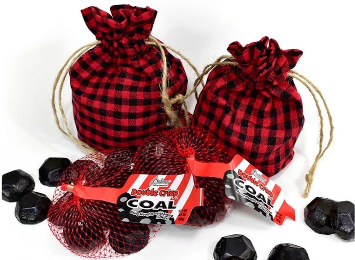 Three red-and-black plaid drawstring bags and two red mesh bags holding black, coal-shaped chocolate candies are displayed, with some candies scattered around them. The mesh bags have labels reading "Double Crisp Coal.