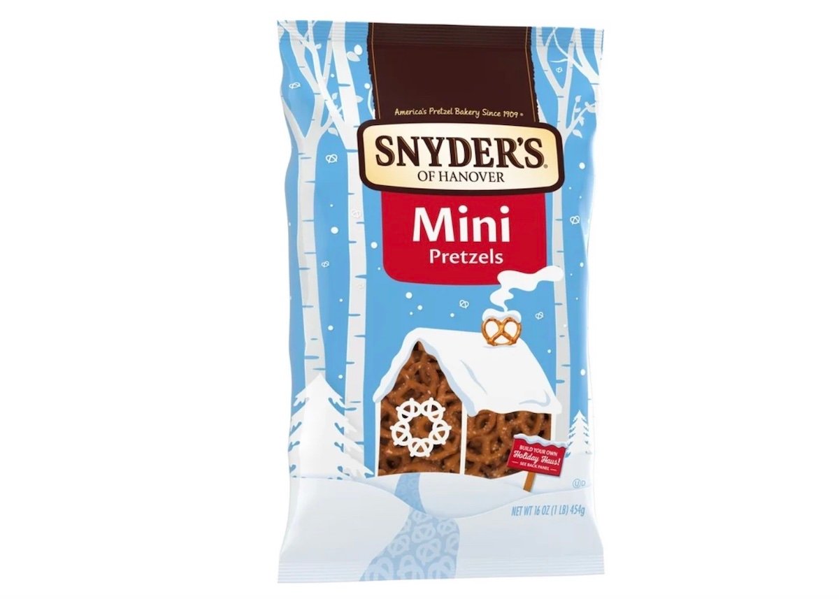 A bag of Snyder’s of Hanover Mini Pretzels with winter-themed packaging, featuring a snow-covered house, pretzels, and falling snowflakes on a blue background.