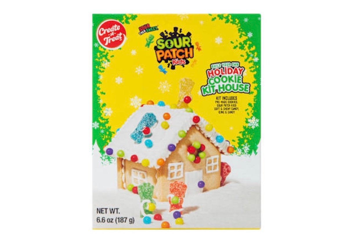 A box of Sour Patch Kids Holiday Cookie Kit House, featuring an image of a decorated cookie house with colorful candy, gumdrops, and Sour Patch Kids on the front against a yellow snowy background. Net weight is 6.6 oz (187 g).