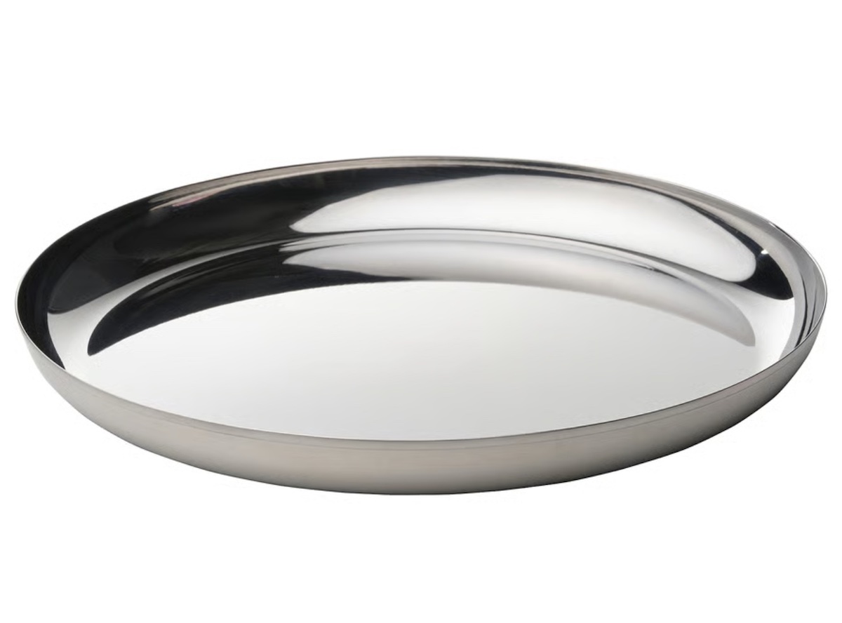 A round, shallow stainless steel plate with smooth, reflective surface, viewed at an angle against a plain white background.