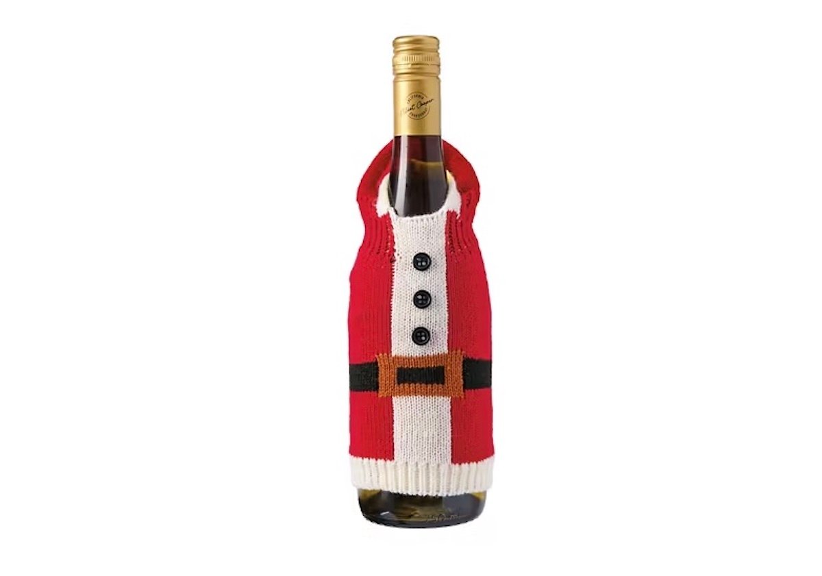 A wine bottle dressed in a red, white, and black knit sweater resembling a Santa Claus outfit, complete with buttons and a belt, against a white background.