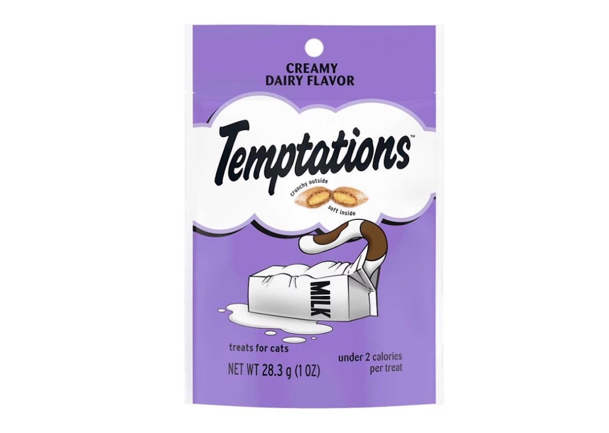 A purple pouch of Temptations Creamy Dairy Flavor cat treats, featuring a cartoon cat reaching into a spilled milk carton. The package highlights "creamy inside" and "under 2 calories per treat.