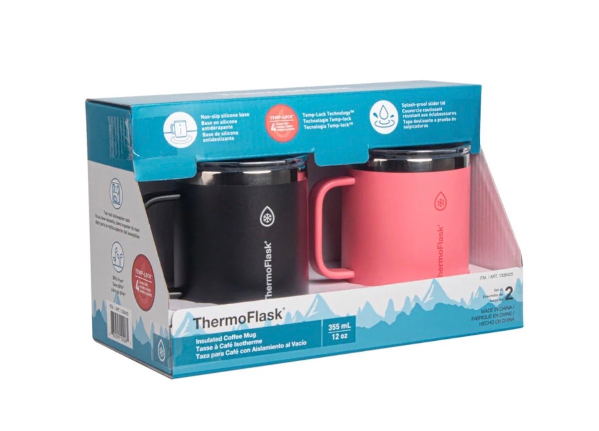 Two insulated ThermoFlask coffee mugs, one black and one pink, are packaged side by side in a blue and white box featuring mountain graphics and product details. Each mug holds 12 oz (355 ml).