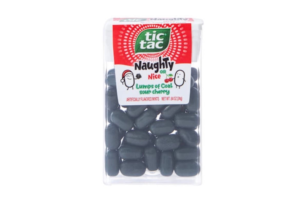 A clear container of Tic Tac mints labeled "Naughty or Nice: Lumps of Coal, sour cherry," showing black-colored mints inside. The label features playful cartoon faces on a red and white background.