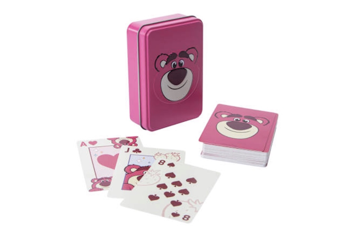 A pink tin box with a bear face design, alongside a matching deck of playing cards. Some cards, including the Ace and Jack of hearts and the eight of spades, are fanned out in front of the box.