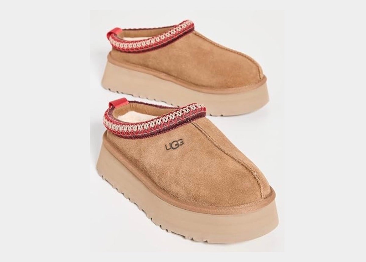 A pair of tan suede slip-on UGG clogs with thick beige soles and red decorative trim around the ankle opening, viewed against a plain light background.
