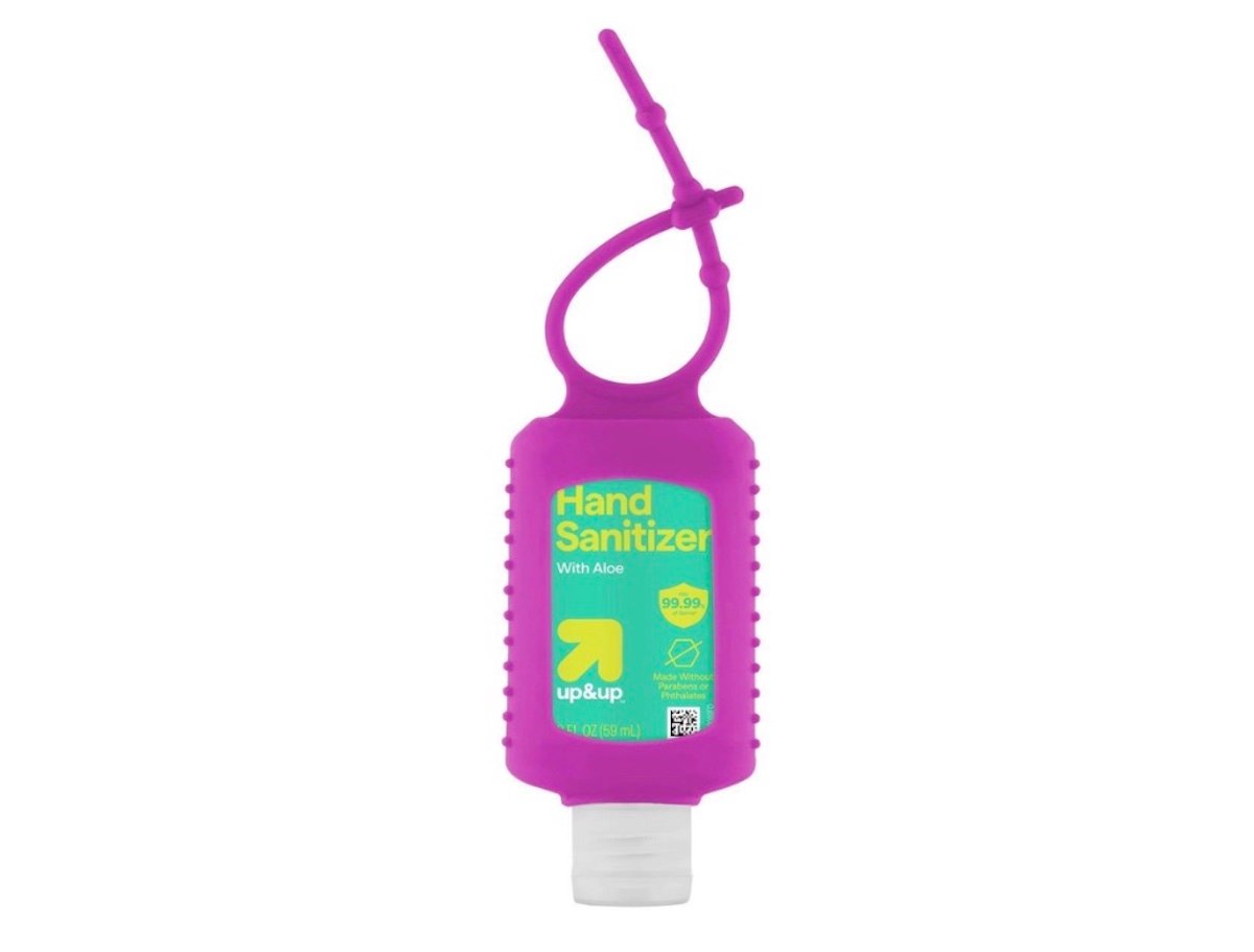 A clear bottle of hand sanitizer with a white cap in a bright purple silicone holder featuring a loop for attachment. The label reads "Hand Sanitizer with Aloe, up & up.