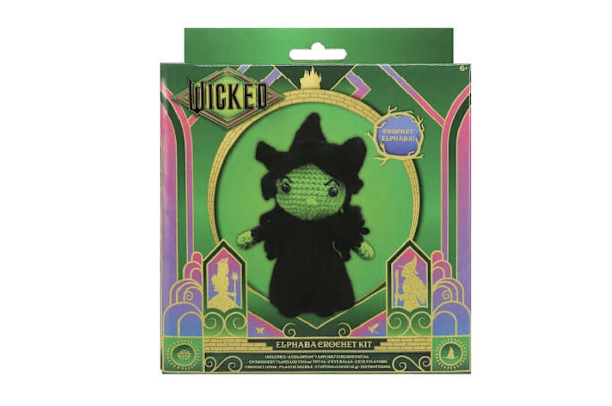 A "Wicked" themed crochet kit featuring Elphaba, shown as a green crocheted doll with a black hat and cape, in a decorative green and gold box with art deco details.
