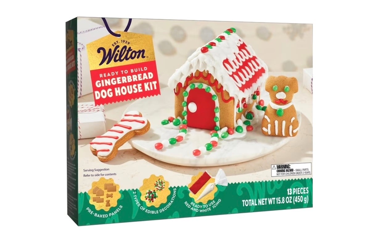 Box of Wilton Gingerbread Dog House Kit showing a decorated gingerbread doghouse with candy details, a bone-shaped cookie, and a gingerbread dog on the front. The kit contains 13 pieces.