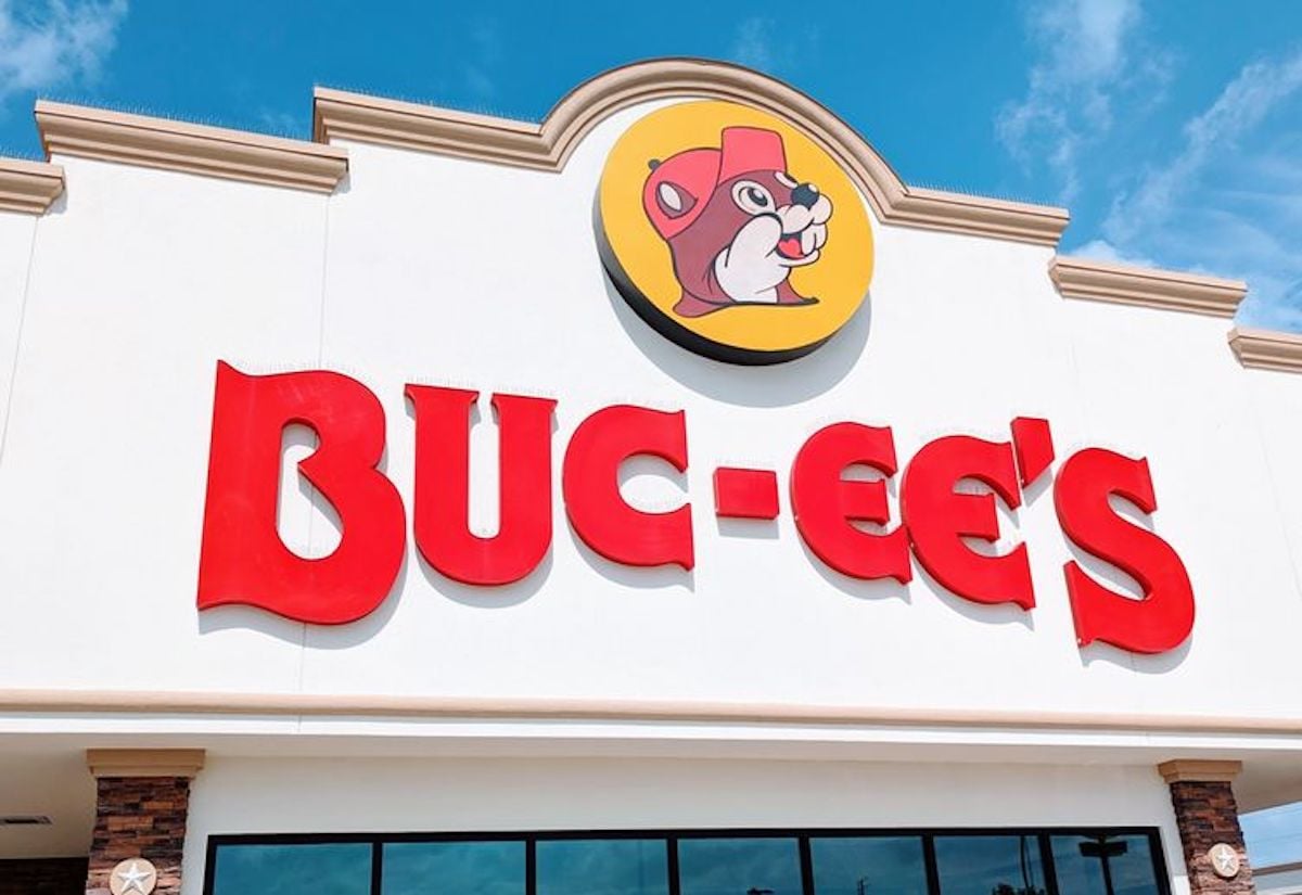 The front of a Buc-ee’s store with large red letters spelling “BUC-EE’S” and a round logo featuring a cartoon beaver wearing a red hat, against a blue sky background.