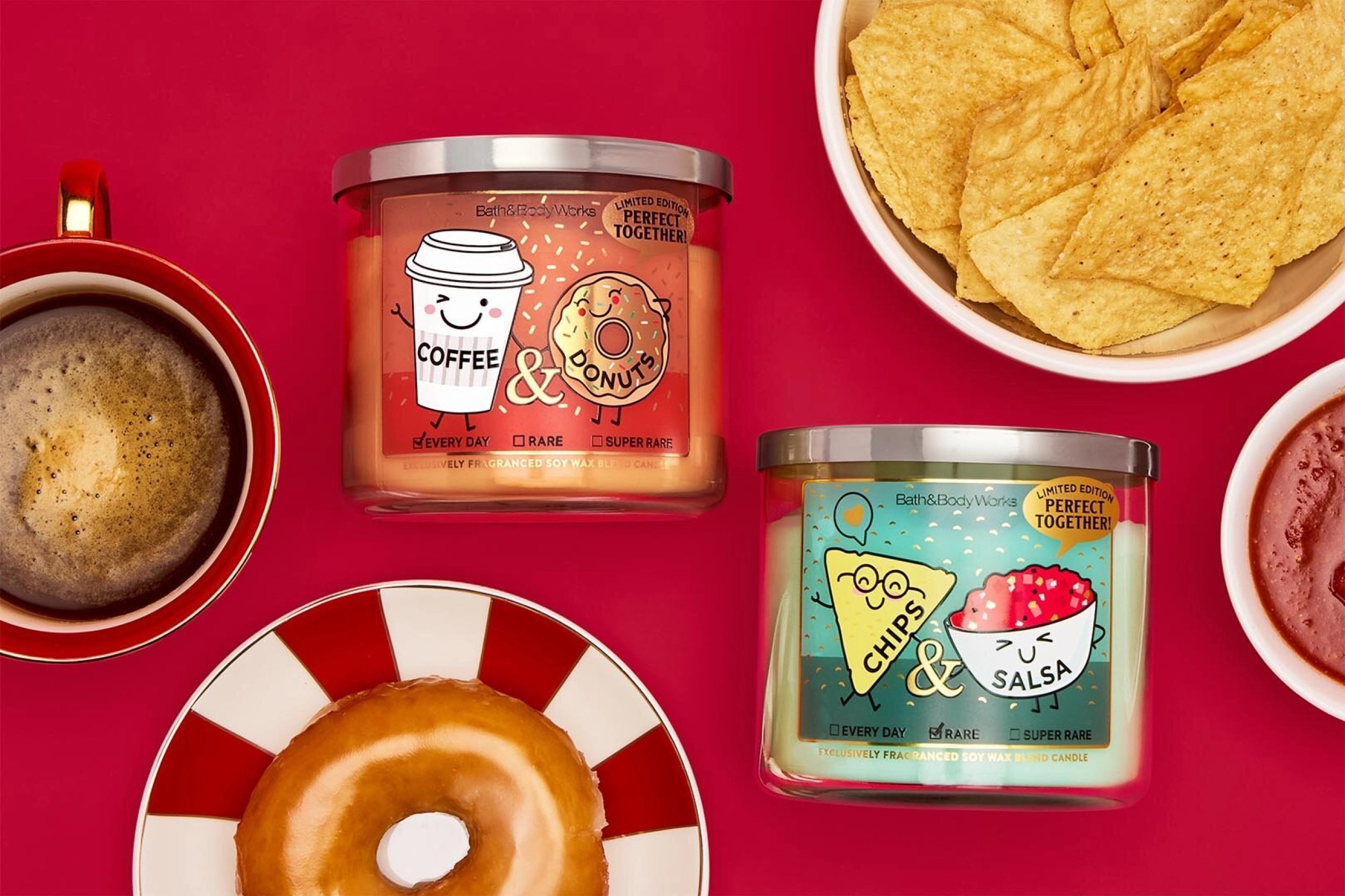 A flat lay of coffee, a donut, tortilla chips, and salsa next to two Bath & Body Works candles labeled "Coffee & Donuts" and "Chips & Salsa," all on a red background. The candles have cute cartoon food illustrations.