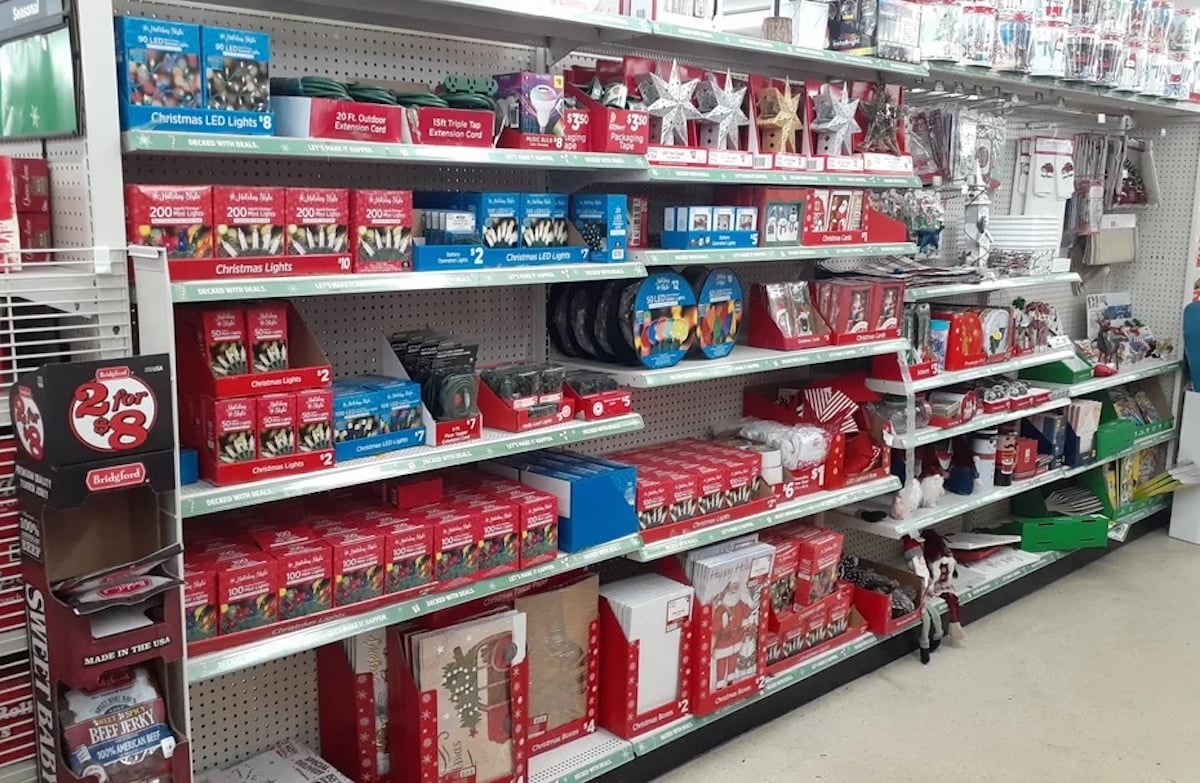 Store shelves are stocked with Christmas decorations, including lights, ornaments, bows, figurines, and gift bags. Most items have red or holiday-themed packaging, creating a festive display.
