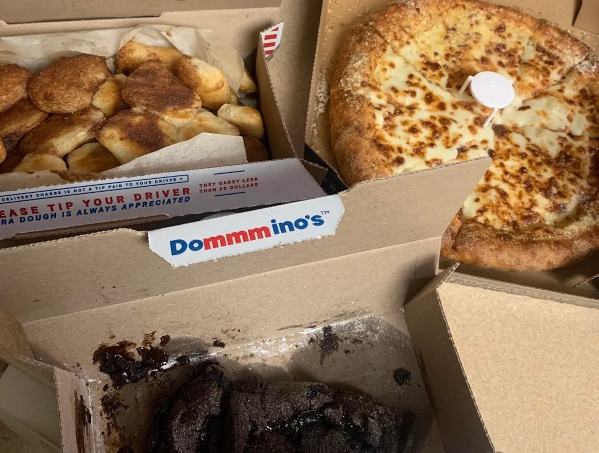 An open pizza box with a cheese pizza, a box of cinnamon bread twists, and a box with chocolate lava cakes from Domino's, all placed on a table.