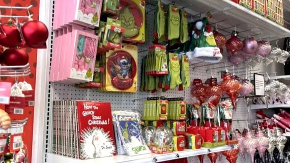 A store display features Dr. Seuss’s “How the Grinch Stole Christmas!” merchandise, including books, socks, mugs, ornaments, and decorations, alongside traditional red and pink Christmas ornaments.
