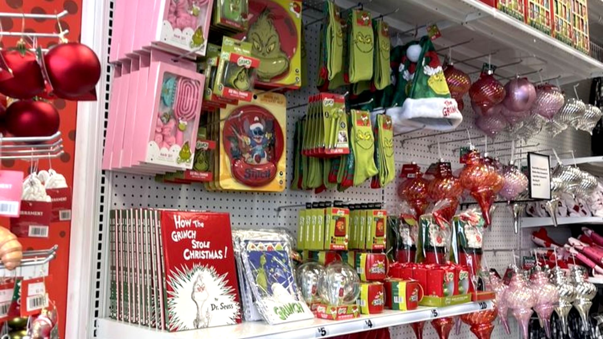 A store display features Dr. Seuss’s “How the Grinch Stole Christmas!” merchandise, including books, socks, mugs, ornaments, and decorations, alongside traditional red and pink Christmas ornaments.