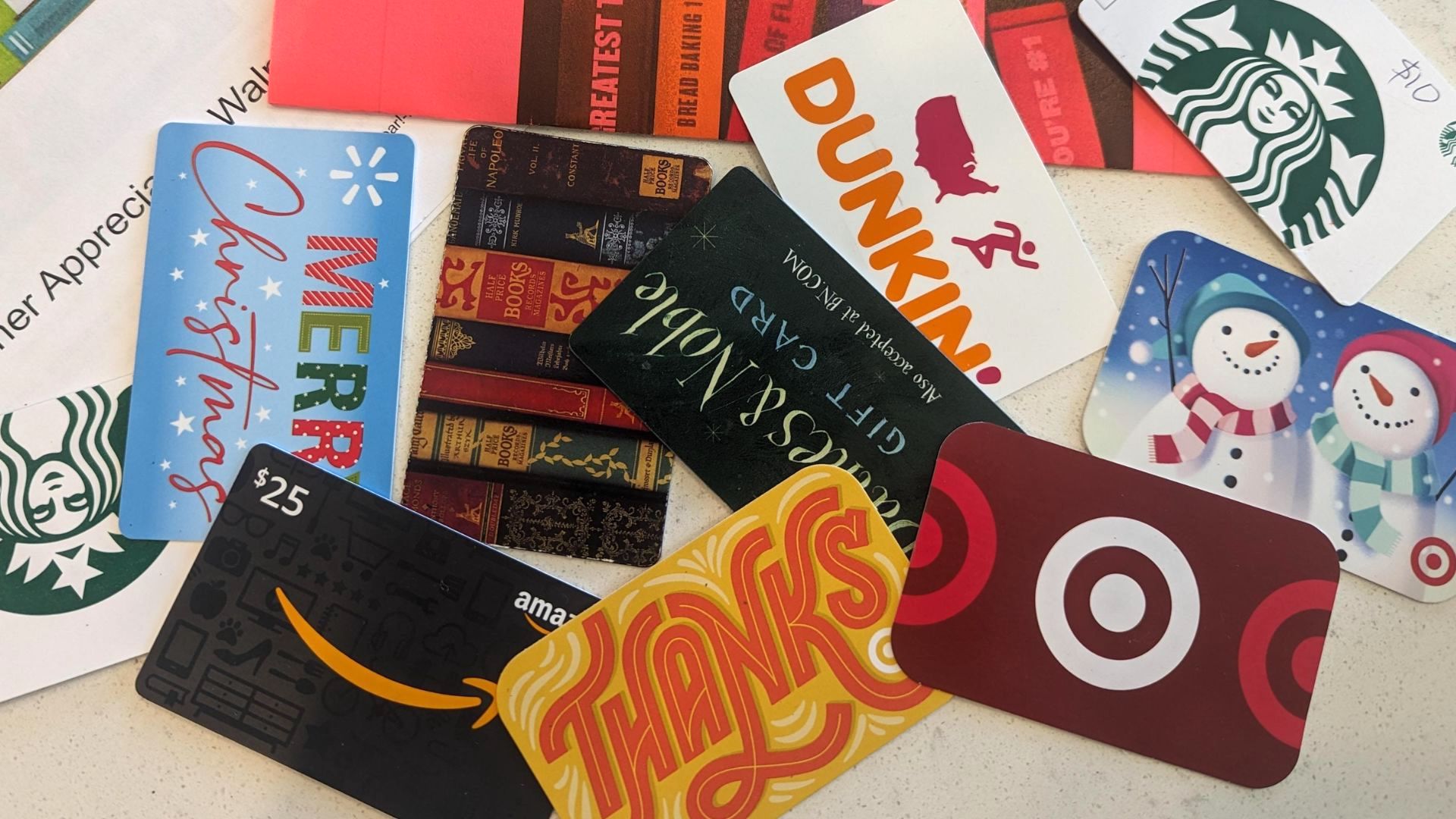 A variety of colorful gift cards, including Starbucks, Amazon, Target, Dunkin', and festive holiday-themed cards, are spread out on a white surface.