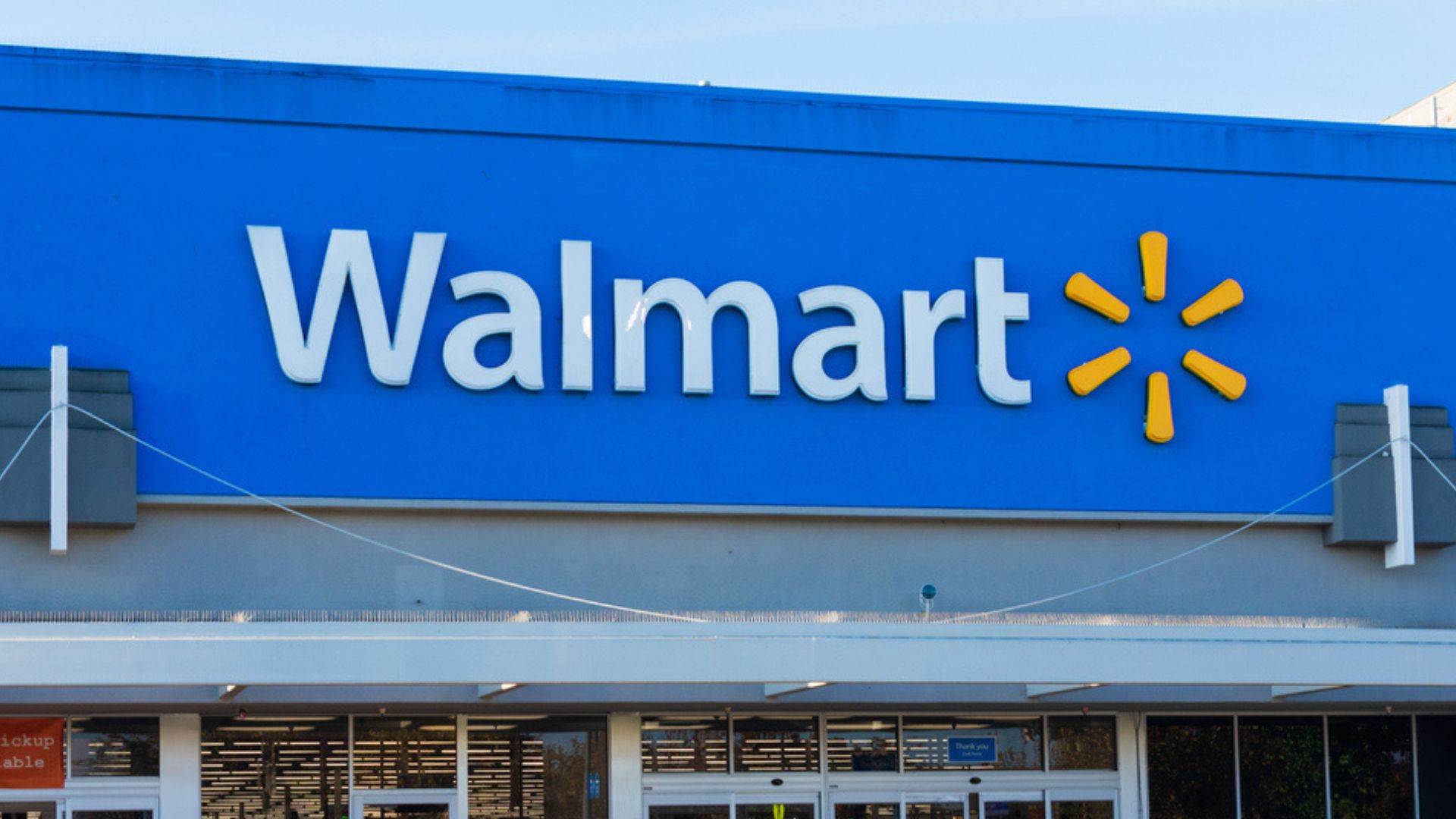 The image shows the front of a Walmart store with the large Walmart logo and yellow spark symbol on a blue background above the entrance.
