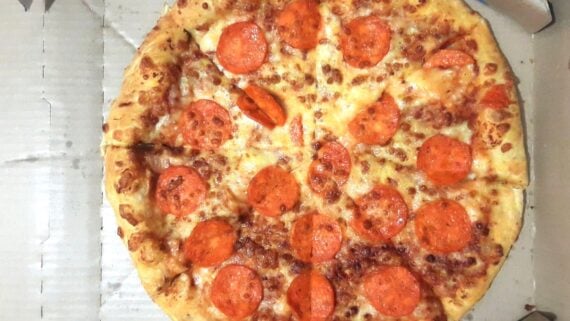 A whole pepperoni pizza with melted cheese and evenly spaced pepperoni slices, viewed from above inside a cardboard pizza box.