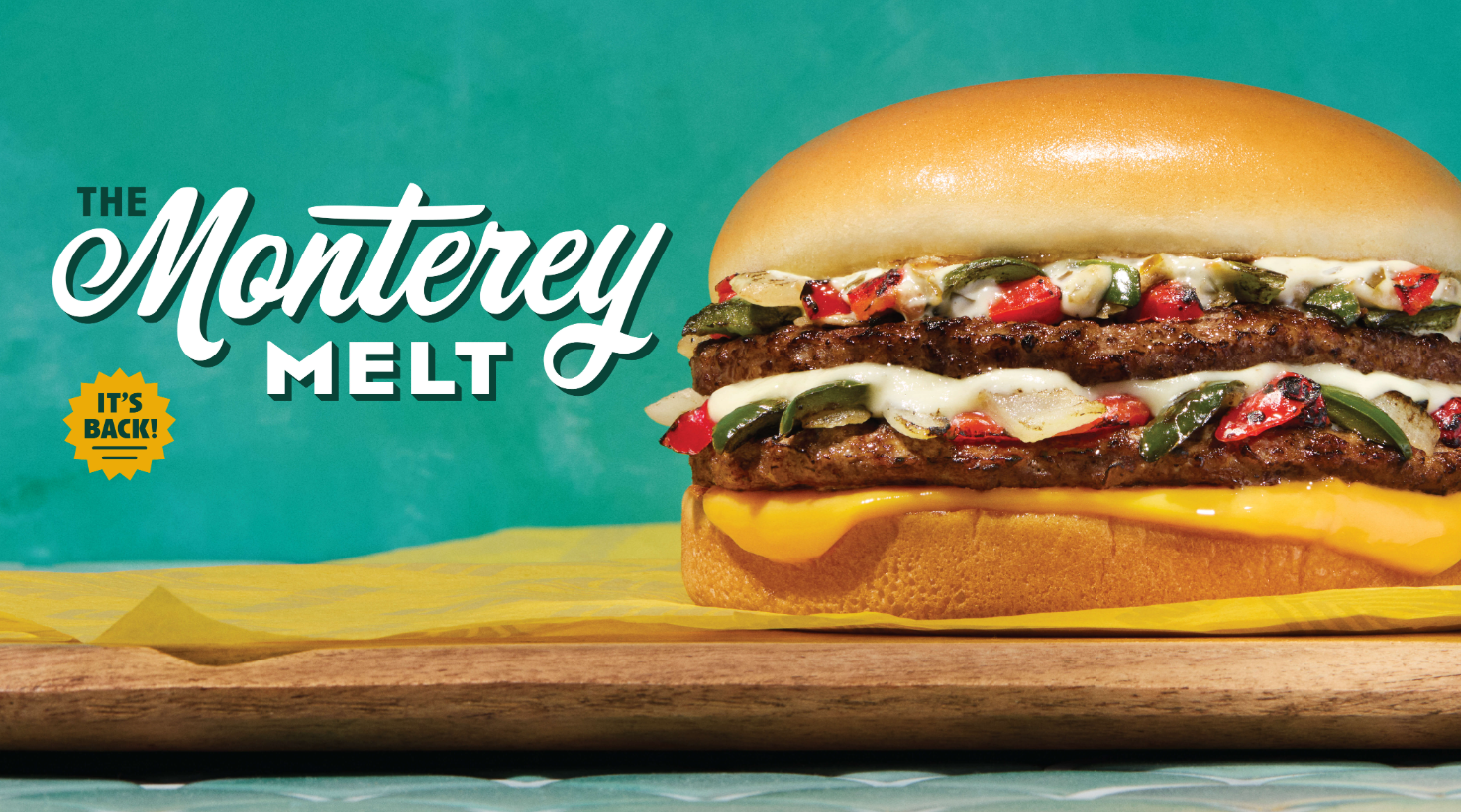 A cheeseburger with two beef patties, melted cheese, peppers, and creamy sauce on a bun sits on a wooden board. Text reads “The Monterey Melt. It’s back on the new fast-food menu!” on a teal background.