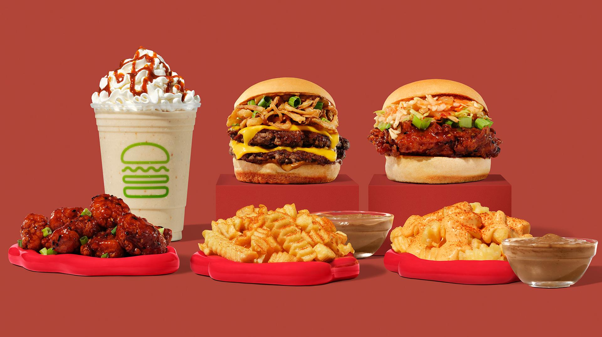 A new fast-food menu features a milkshake with whipped cream, two burgers, sauced fried chicken bites, crinkle-cut fries, mac and cheese, and dipping sauces—all arranged on a vibrant red background.
