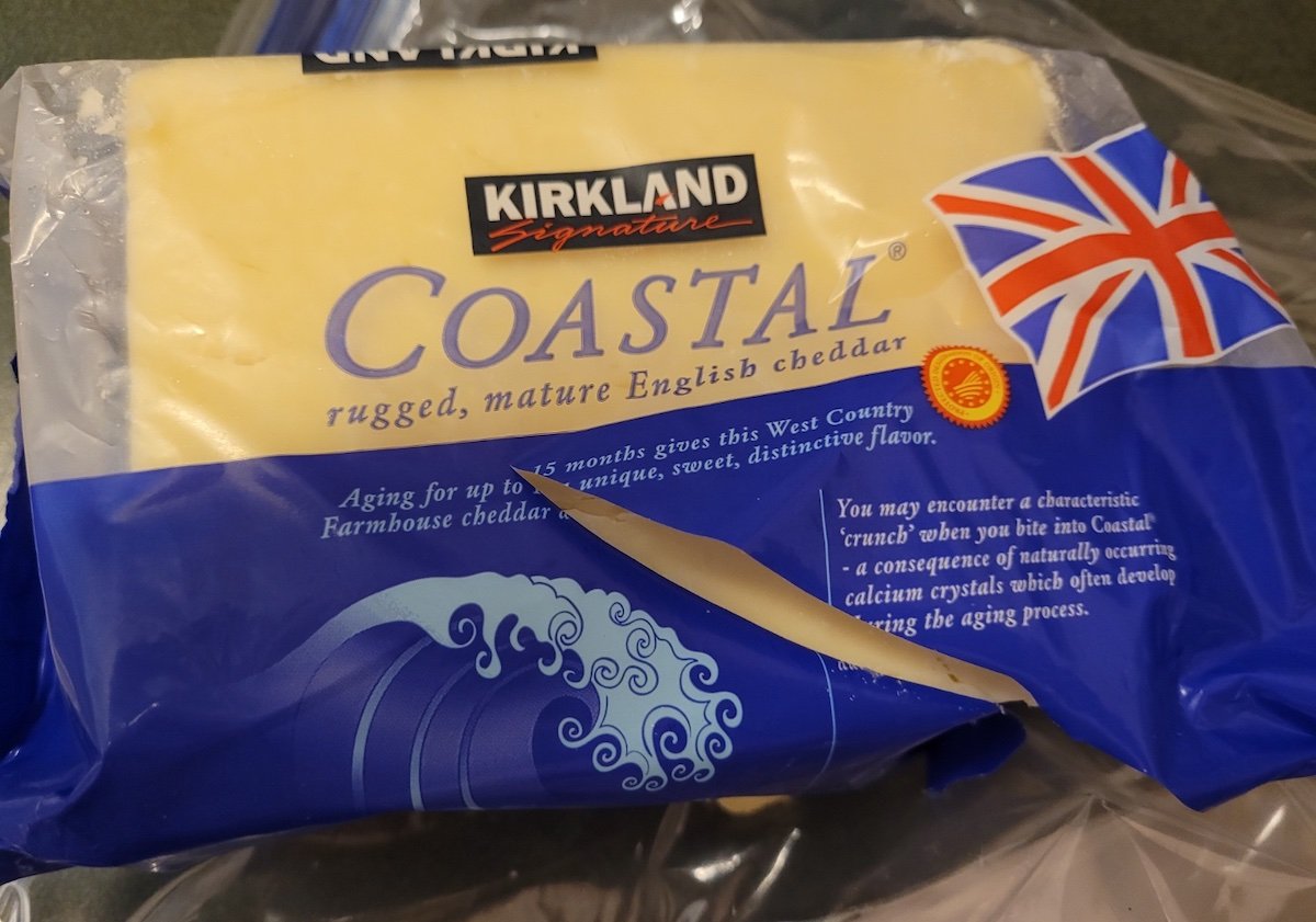 A package of Kirkland Signature Coastal mature English cheddar cheese, wrapped in blue and white packaging with a British flag and text describing its aging process and flavor characteristics.