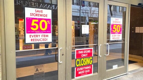 Storefront glass doors with bright signs reading "Save Storewide Up to 50% Off", "Every Item Reduced!", and "This Store Only Closing, Everything Must Go!" Interior of the store is visible through the doors.