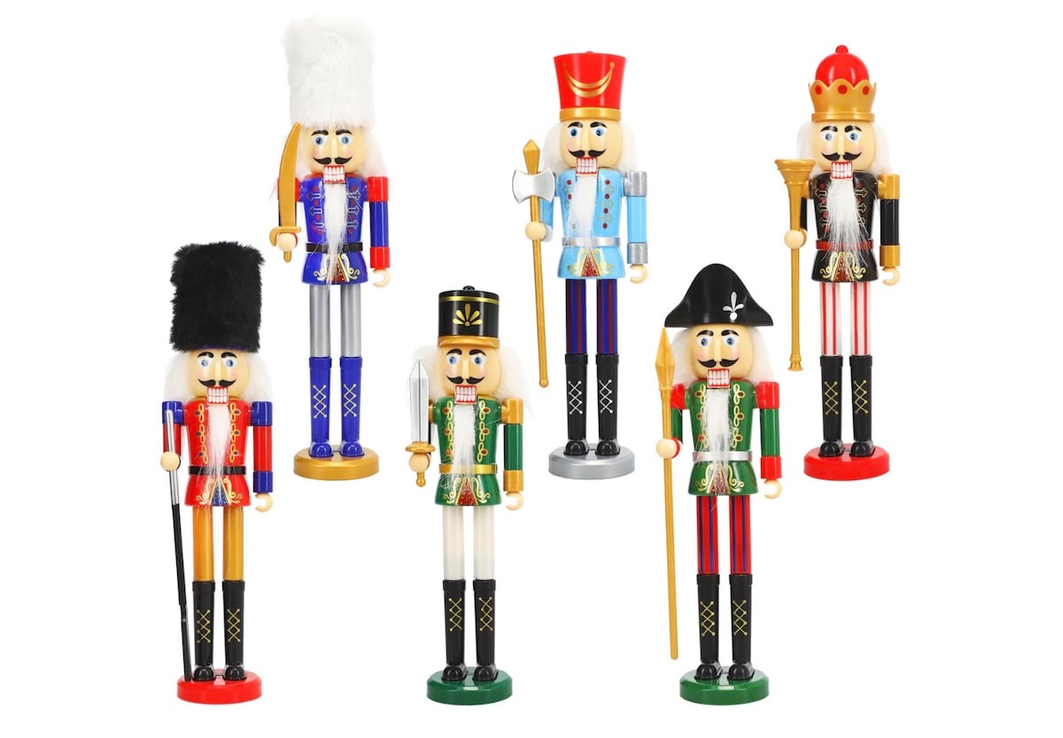 Six colorful wooden nutcracker figurines are dressed in various festive soldier and royal outfits, each with distinct hats and accessories, standing upright against a white background.