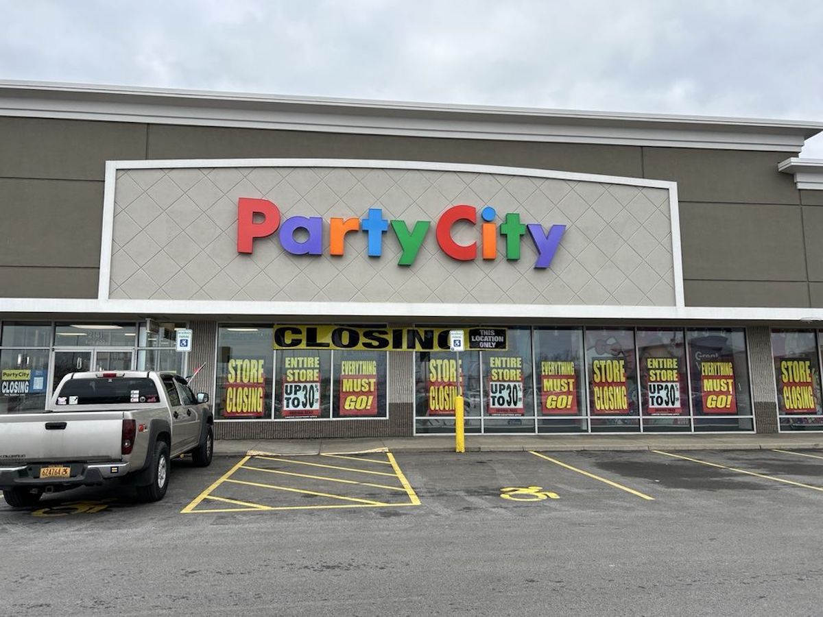 A Party City store with signs in the windows reading "STORE CLOSING," "ENTIRE STORE UP TO 70% OFF," and "STORE MUST GO!" Two vehicles are parked outside in a mostly empty parking lot.