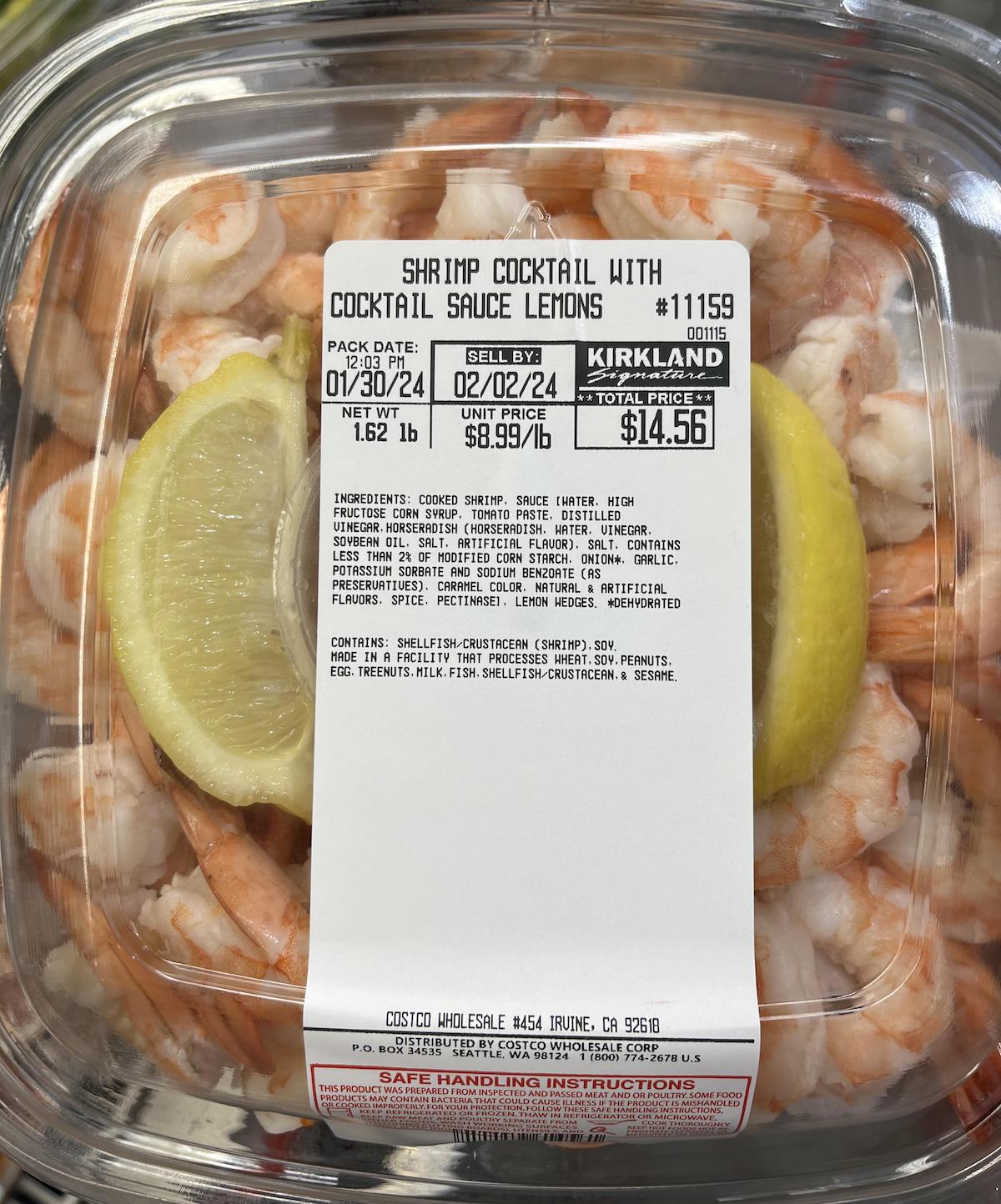 A clear plastic container of Kirkland shrimp cocktail with two lemon slices and a white label detailing ingredients, price, weight, and safe handling instructions.