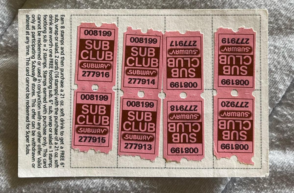 A sheet of six pink Subway Sub Club stamps is attached to a card with printed instructions on a textured gray surface. The stamps are arranged in two rows of three, some facing upside down.