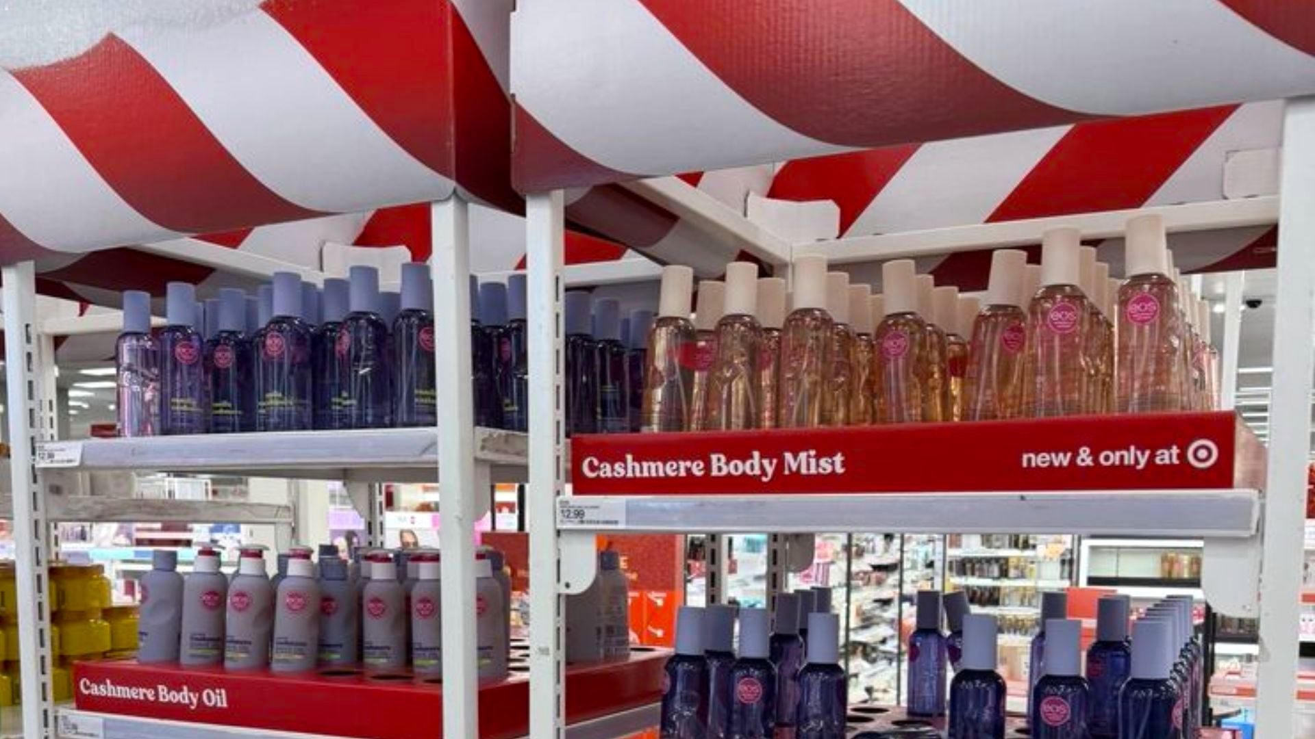 Shelves at a store display bottles of Cashmere Body Mist and Body Oil under a red and white striped awning. A sign reads “new & only at Target.” The display is neatly organized with multiple rows of products.