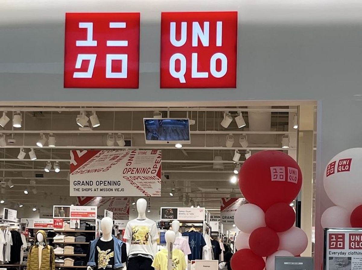 The entrance of a UNIQLO clothing store with red and white signage, mannequins displaying outfits, and large red and white balloons inside for a grand opening event.