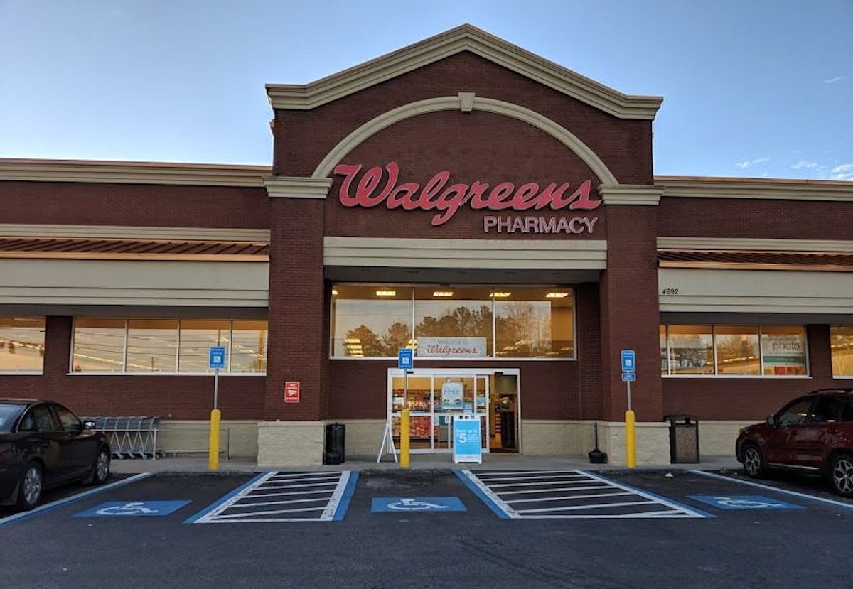 Exterior view of a Walgreens Pharmacy store with large red signage, accessible parking spaces in front, and shopping carts near the entrance on a clear day.